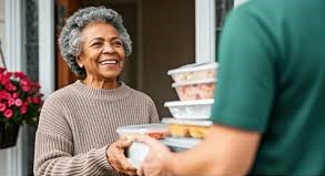 A smiling senior woman receiving prepared meals at her front door