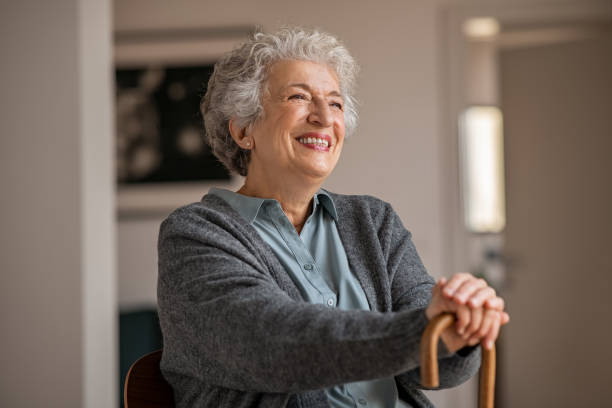 A smiling senior woman resting her hands on a wooden cane